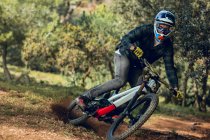 Unrecognizable man looking at camera in helmet, gloves and protection glasses jumping doing whip trick downhill during mountain biking practice in wood forest — Stock Photo