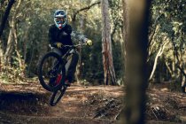 Unrecognizable man in helmet, gloves and protection glasses jumping doing whip trick downhill during mountain biking practice in wood forest — Stock Photo