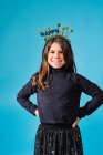 Happy preteen in black and gold headgear with wishes happy New Year smiling at camera with hands on hips against light blue background in modern studio — Stock Photo