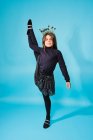 Trendy zufriedenes Kind in Silvesterkopfbekleidung und schwarzer Kleidung blickt in die Kamera und macht vor hellblauem Hintergrund im Studio stehend Split-Übungen — Stockfoto