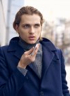 Des seriösen jungen Geschäftsmannes im eleganten Mantel, der sein Handy benutzt, während er auf der Steintreppe der Stadtstraße steht — Stockfoto
