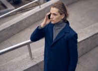 Von oben ein seriöser junger Geschäftsmann im eleganten Mantel, der auf der steinernen Treppe der Stadtstraße steht und die Nachricht auf dem Handy checkt — Stockfoto
