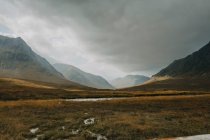 Paisagem escocesa com estreito rio curvilíneo fluindo entre coberto com colinas de grama sob céu nublado no dia de outono — Fotografia de Stock