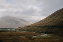 Paesaggio scozzese con stretto fiume curvy che scorre tra coperto di colline erbose sotto cielo nuvoloso in autunno giorno — Foto stock