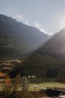 Paisaje tranquilo de la campiña escocesa con pastizales amarillos y casita solitaria situada cerca de la montaña rocosa contra el cielo nublado - foto de stock