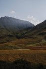 Спокойный пейзаж шотландской сельской местности с желтыми лугами в скалистой горе против облачного неба — стоковое фото