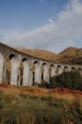 Angolo basso di vecchio viadotto ferroviario in altopiano scozzese contro le montagne e cielo nuvoloso blu in autunno giorno — Foto stock