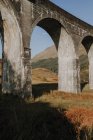 Bajo ángulo del viejo viaducto ferroviario en las tierras altas escocesas contra las montañas y el cielo azul nublado en el día de otoño - foto de stock