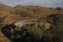 Desde arriba viejo viaducto ferroviario en las tierras altas escocesas contra las montañas y el cielo azul nublado en el día de otoño - foto de stock