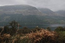 Paisagem nebulosa de cordilheira coberta com nevoeiro e nuvens perto do lago calmo no planalto escocês — Fotografia de Stock