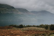 Misty landscape of mountain range covered with fog and clouds near calm lake in Scottish highland — Stock Photo