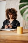 Empresária retro positivo com cabelo encaracolado sentado à mesa e usando smartphone no escritório — Fotografia de Stock