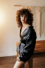 Sensual female manger in leather skirt suit and bra smiling for camera and touching curly hair during work — Stock Photo