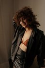 Sensual woman in leather jacket and bra with curly hair in room — Stock Photo