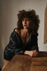 Sensual woman in leather jacket and bra with curly hair in room — Stock Photo