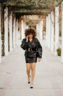 Femme entrepreneur en tenue vintage marchant sur le chemin de l'asphalte et ayant une conversation smartphone tout en se rendant au travail à travers le parc de la ville — Photo de stock