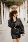Жінка-підприємець повного тіла в старовинному вбранні, що йде асфальтовим шляхом і веде розмову зі смартфонами під час роботи через міський парк — стокове фото