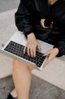Зверху бізнес-леді в чорному шкіряному вбранні, що сидить на кордоні і переглядає дані про ноутбук під час роботи над віддаленим проектом на міській вулиці — стокове фото