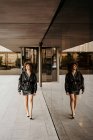 Femme manager en costume jupe en cuir noir regardant loin tout en marchant près du bâtiment avec mur de verre sur la rue de la ville — Photo de stock