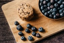From above composition with stacked cookies and fresh blueberry placed on wooden cutting board on table — Stock Photo