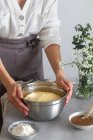 Unrecognizable female in gray apron putting bowl with fresh dough on table near flour and apple puree while preparing pastry — Stock Photo
