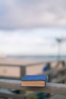 Von oben geschlossenes Buch mit blauem Einband auf Holzzaun bei sonnigem Tag mit Strand im Hintergrund — Stockfoto