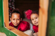 Симпатичні чорні маленькі брати і сестри посміхаються і дивляться на камеру через відкрите вікно дерев'яної кабіни — стокове фото