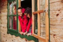 Симпатичные черные маленькие братья и сестры улыбаются через открытое окно деревянной каюты — стоковое фото