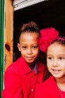 Симпатичные черные маленькие братья и сестры улыбаются и смотрят на камеру через открытое окно деревянной каюты — стоковое фото