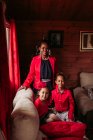Весела молода чорна жінка з милими смішними братами і сестрами в червоному одязі, дивлячись на камеру, проводячи час разом у затишному заміському будинку — стокове фото