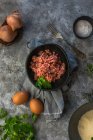 Da sopra vista dall'alto cipolle crude, uova ed erbe poste sul tavolo grigio vicino alla ciotola con carne macinata sale in cucina — Foto stock