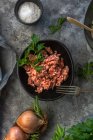 Desde arriba ver cebollas crudas y hierbas colocadas en la mesa gris cerca del tazón con sal de carne picada en la cocina - foto de stock