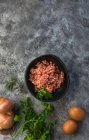 De cima vista superior cebolas cruas, ovos e ervas colocadas em mesa cinza perto tigela com sal de carne picada na cozinha — Fotografia de Stock