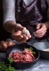 From above unrecognizable person wearing apron showing meatball to camera over bowls with minced meat and bread crumbs during lunch preparation — Stock Photo