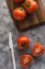 Гофровані і цілі свіжі помідори кладуть дерев'яну дошку на грубий сірий стіл під час приготування їжі на кухні — стокове фото