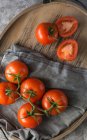 Tomates fraîches coupées en deux et entières placées sur une table grise rugueuse pendant la préparation des aliments dans la cuisine — Photo de stock