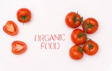 From above top view clean ripe tomato placed near organic food writing on while background — Stock Photo