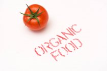 De dessus vue propre tomate mûre placée près des aliments biologiques écriture sur tandis que le fond — Photo de stock