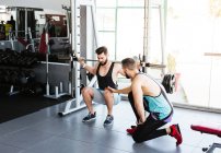 Powerful determined sportsman doing exercise with barbell at squat rack during weightlifting training with personal coach in modern gym — Stock Photo
