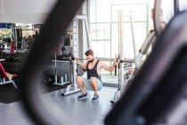Powerful determined sportsman doing exercise with barbell at squat rack during weightlifting training with personal coach in modern gym — Stock Photo