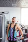 Homem barbudo muscular em sportswear olhando para a câmera enquanto de pé com os braços cruzados e apoiando-se em equipamentos esportivos na luz ginásio contemporâneo — Fotografia de Stock