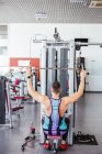 From above back view of unrecognizable sportsman in sports clothes performing exercise on weight machine against blurred interior of contemporary sport club — Stock Photo