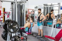 Confident instructor helping diligent client in sports clothes performing exercise on weight machine while standing against blurred interior of modern sport center — Stock Photo