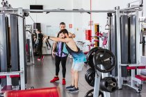 Confident instructor helping diligent client in sports clothes performing exercise on weight machine while standing against blurred interior of modern sport center — Stock Photo