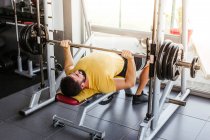 High angle of calm sportsman in activewear performing exercise with barbell while laying on bench near window wall in modern sports center — Stock Photo
