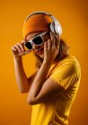 Glückliche junge Frau in heller Kleidung, die stylische Sonnenbrille aufsetzt und lächelt, während sie Musik vor orangefarbenem Hintergrund hört — Stockfoto