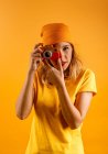 Счастливая молодая женщина смотрит в камеру, держа в руках фальшивую деревянную винтажную фотокамеру, стоящую на жёлтом фоне — стоковое фото