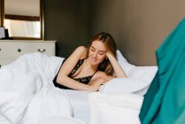 Pretty young female in underwear lying down in bed smiling with closed eyes in morning in cozy bedroom at home — Stock Photo