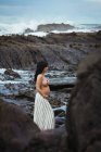Мрійлива топлес брюнетка красива вагітна жінка в спідниці максі, що стоїть на чудових каменях з струмком і покриває груди, дивлячись геть — стокове фото