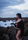 Side view of happy sensual pregnant woman looking away wearing long waving lingerie robe walking with bare belly on rocky coast in gloomy day — Stock Photo